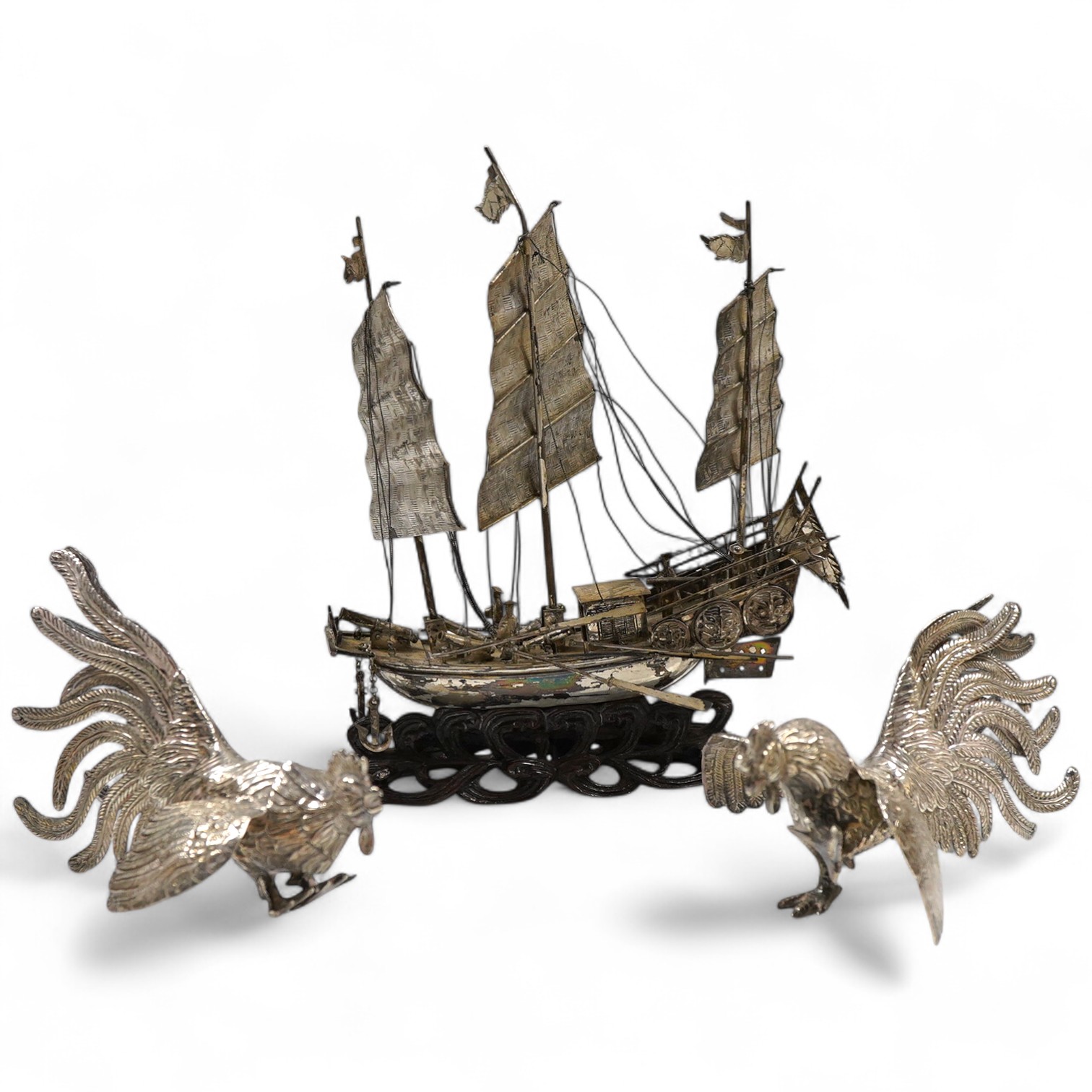 A pair of modern silver fighting cocks, import marks for Sheffield, Assay Office, Sheffield, 1977, height 68mm, together with a Chinese white metal miniature model of a ship, on a carved hardwood base, overall height 20.